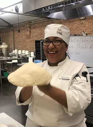 Park City Culinary Institute student Connie tossing dough and smiling.